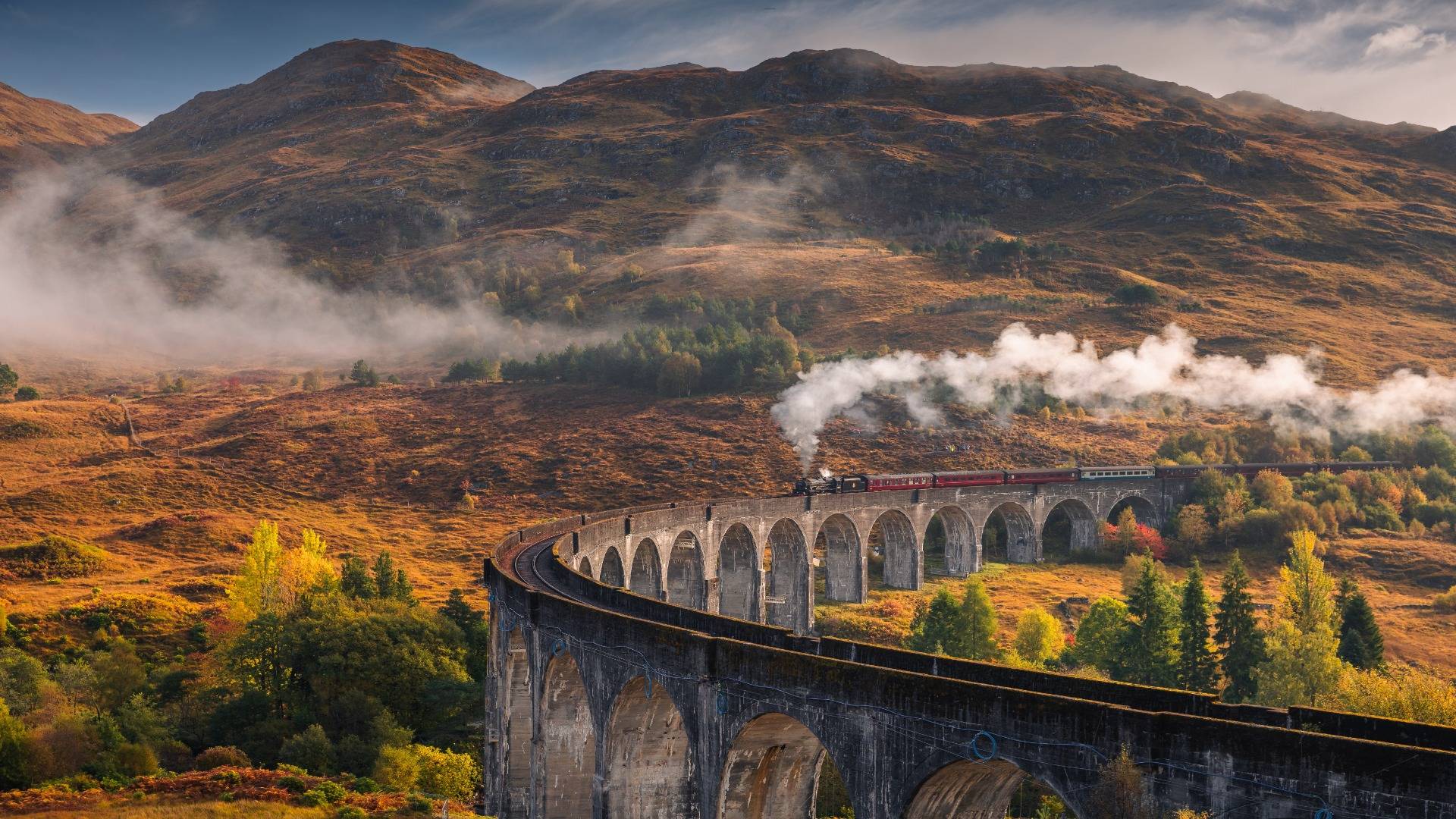 Steam train crossing the Glennfinnan Viaduct on an autumn morning