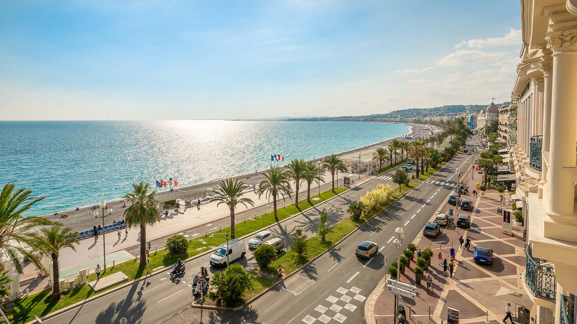The sunny, palm-tree lined Promenade Des Anglais in Nice, France, next to the sparkling sea