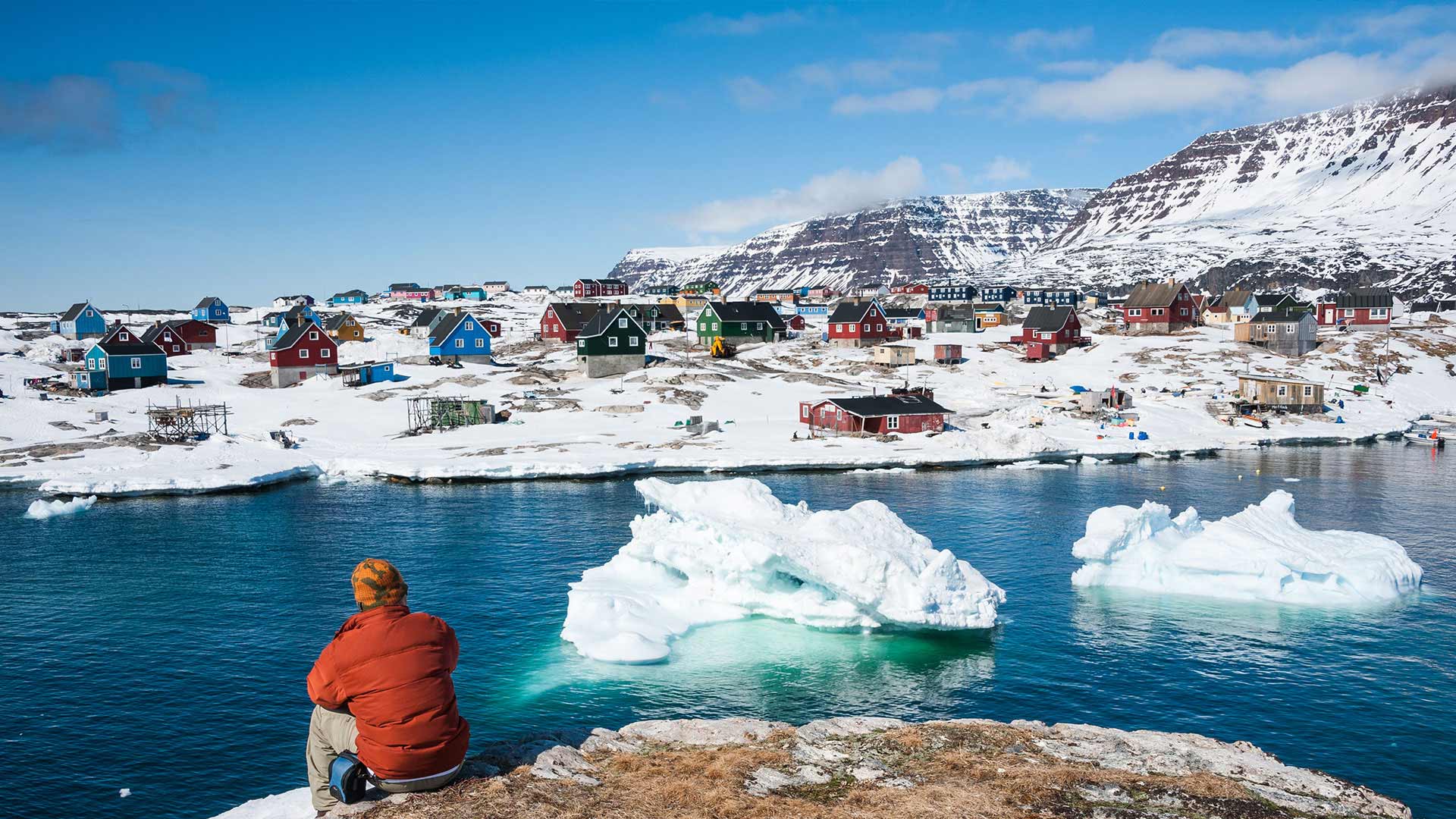 Person looking out over the icebergs and colourful houses of Qeqertarsuaq, Greenland
