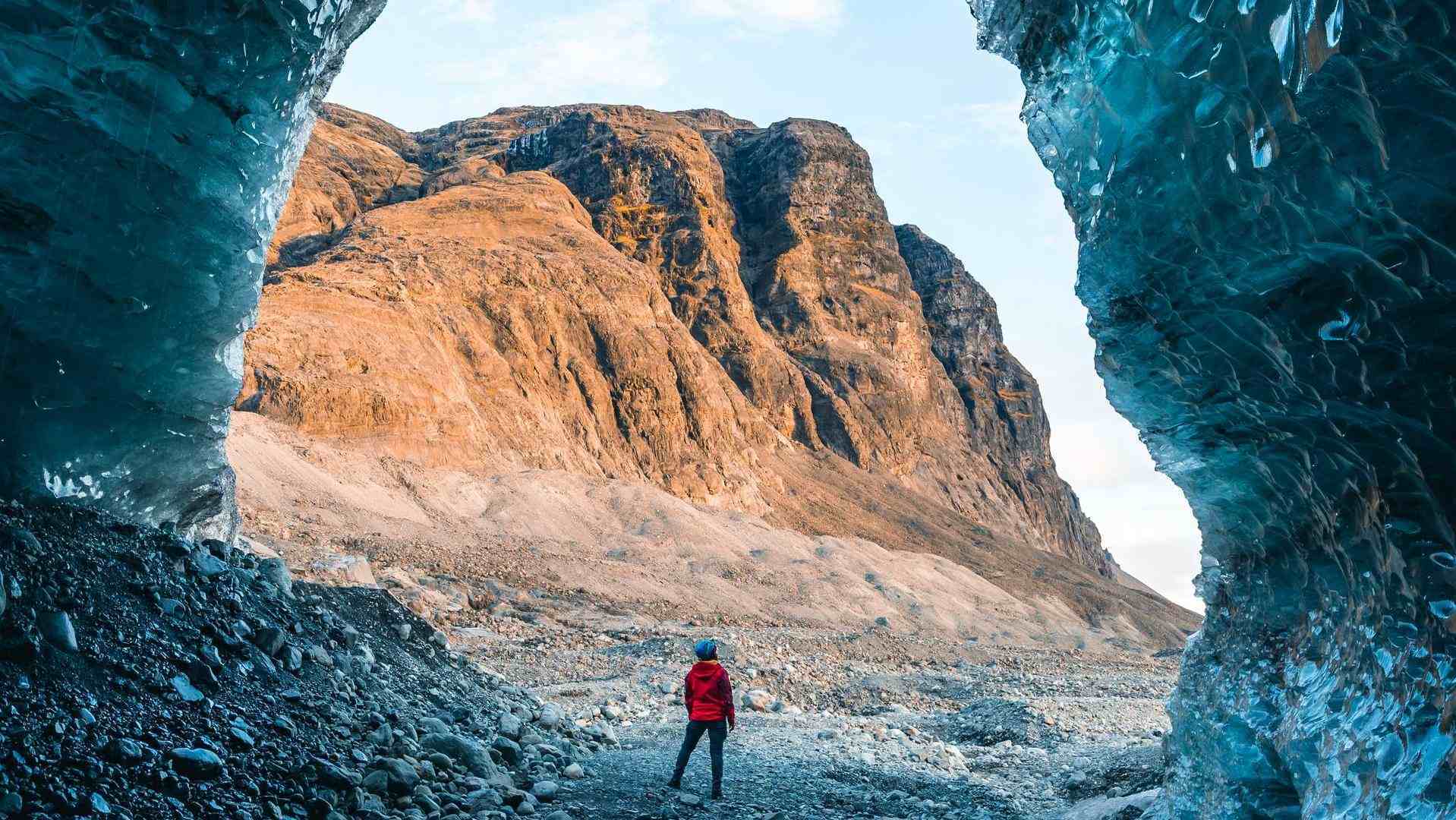 A person admiring an icy ceiling with a sunny mountain backdrop.