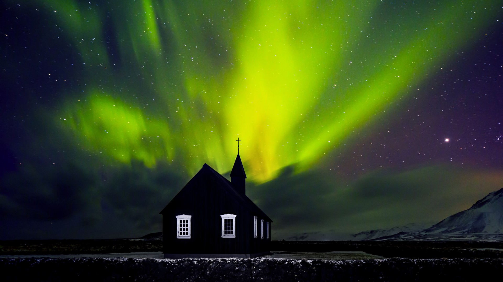 Green northern lights over a black church in Iceland