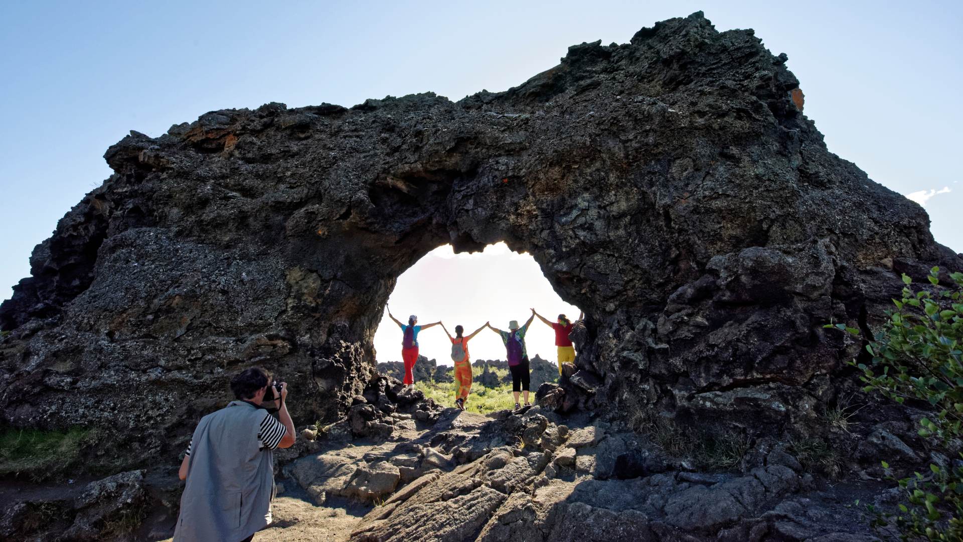 Friends jumping underneath a towering rock arch.