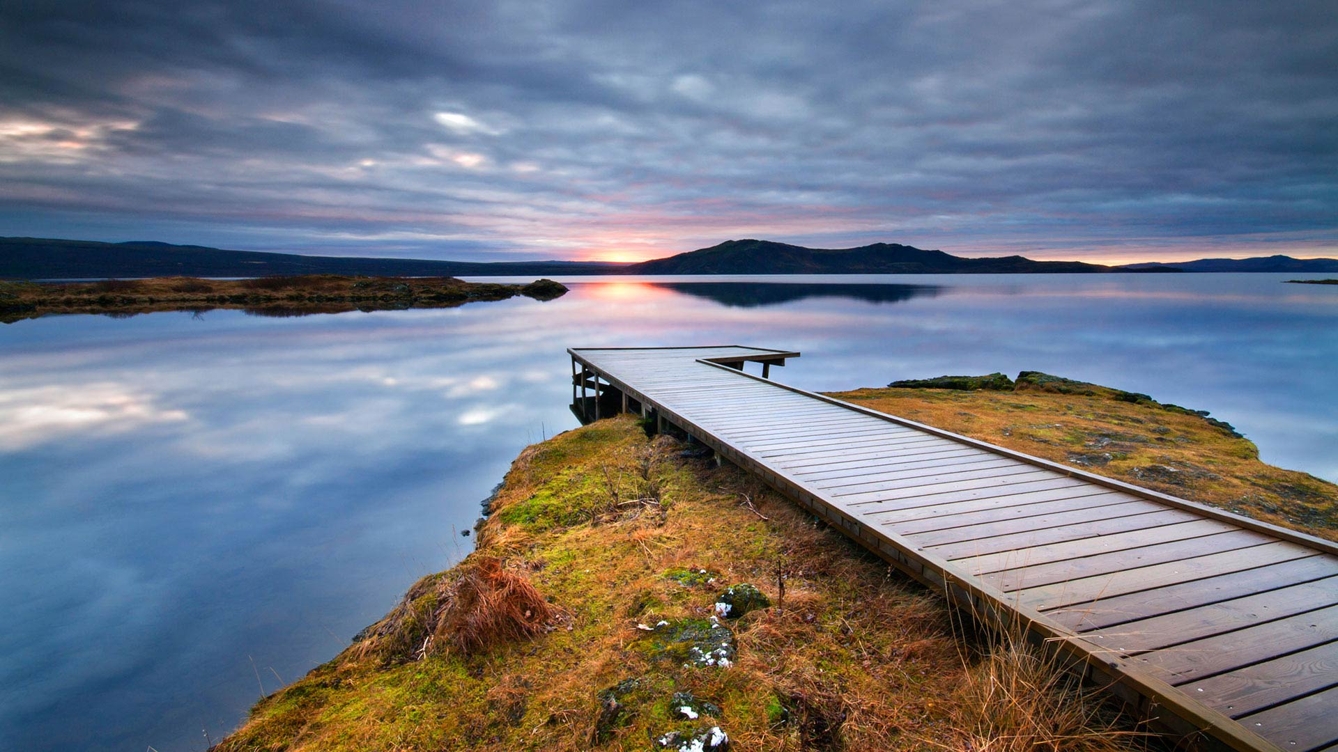 A still lake with a wooden walkway leading towards it.