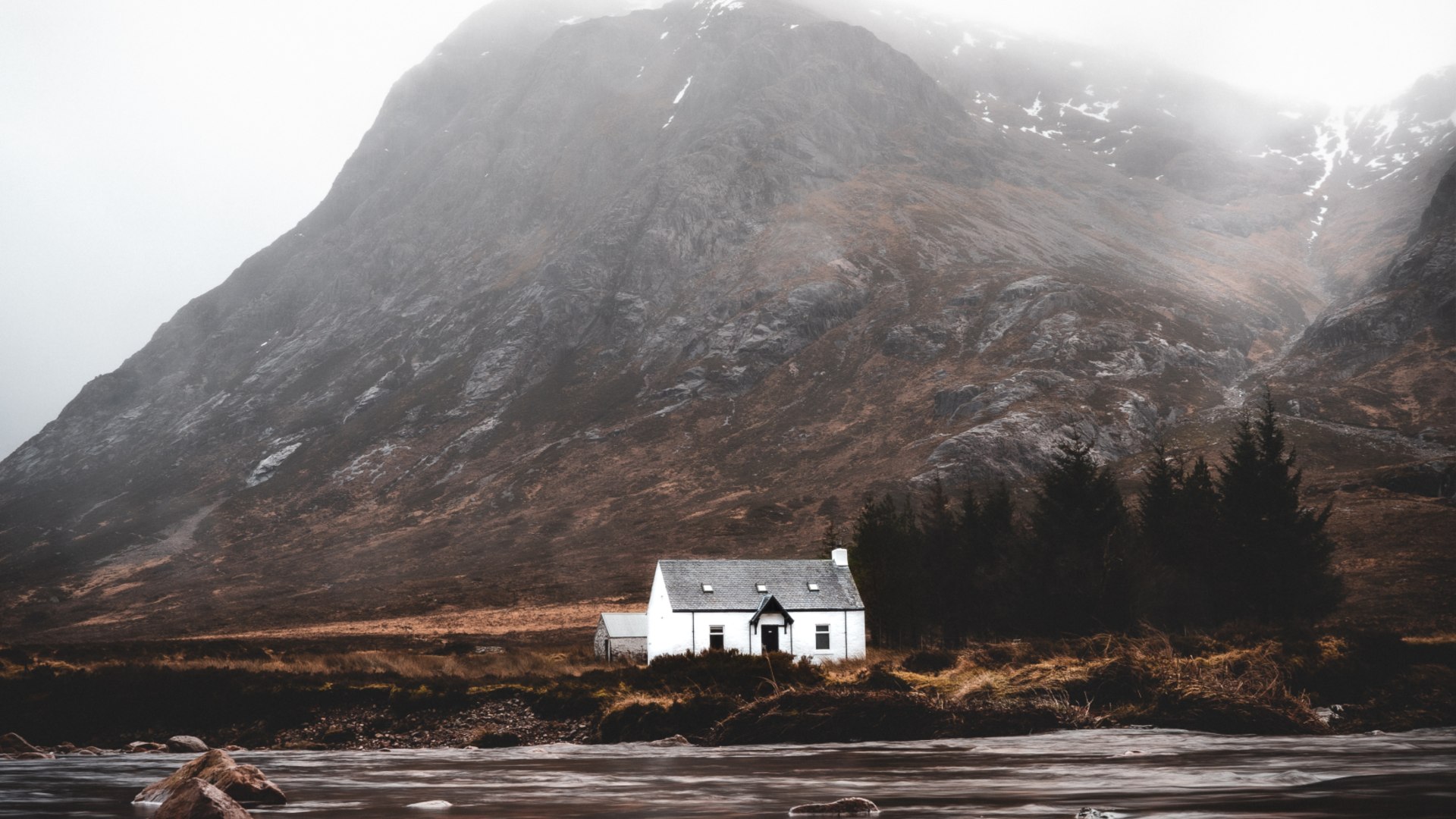 A white house in front of a misty, mountain backdrop in Glen Coe