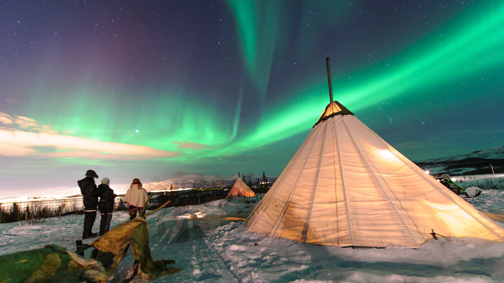people sitting amidst sami tents with northern lights above