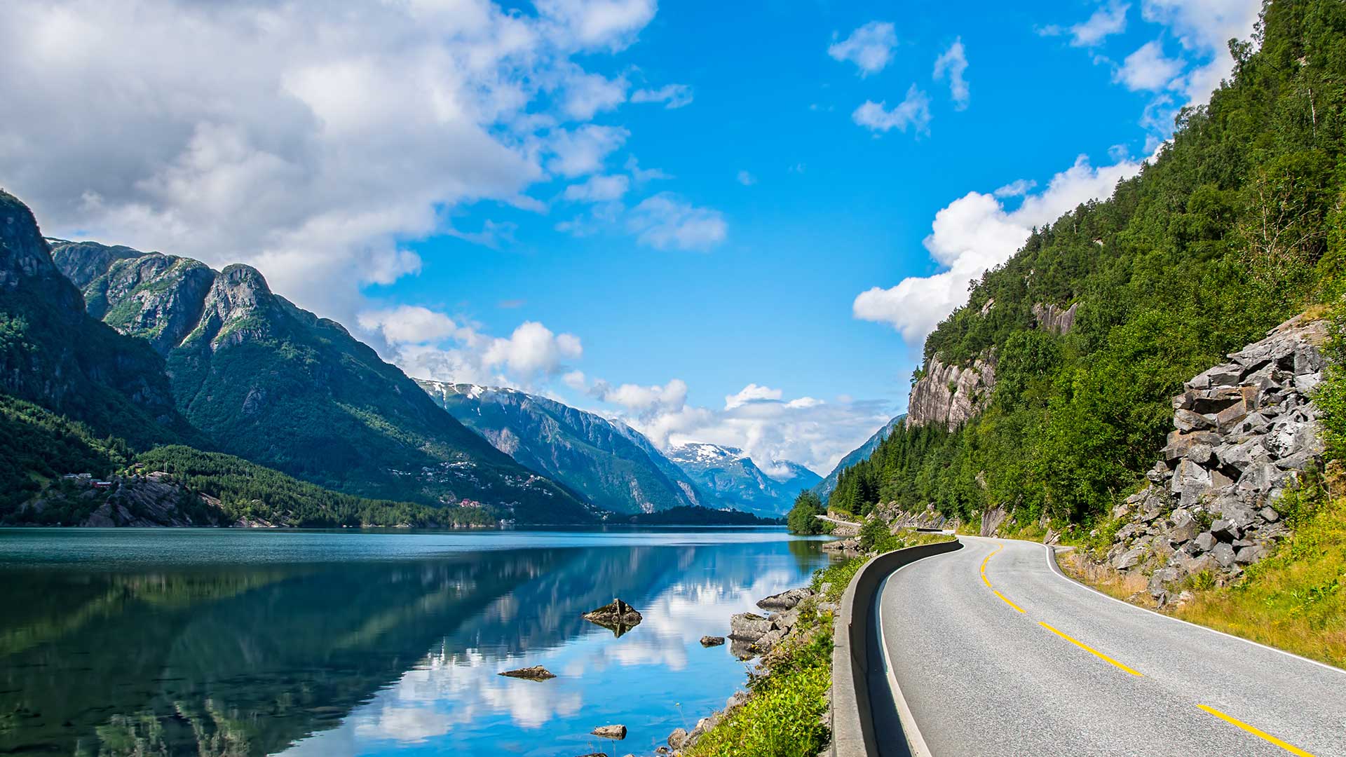 A road hugging the glistening fjords with bright a bright blue sky