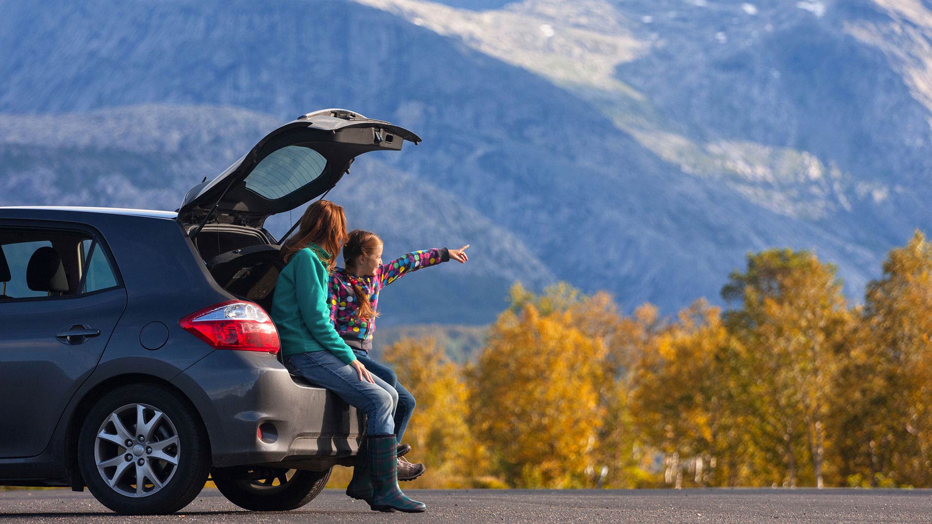 mother and daughter sitting in a car amidst autumn foliage