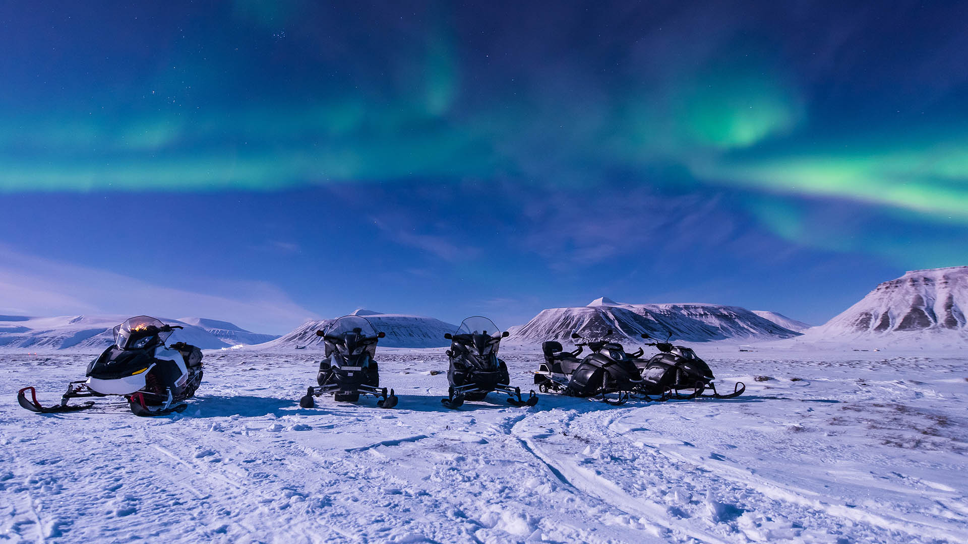 Snowmobiles under the northern lights outside Longyearbyen