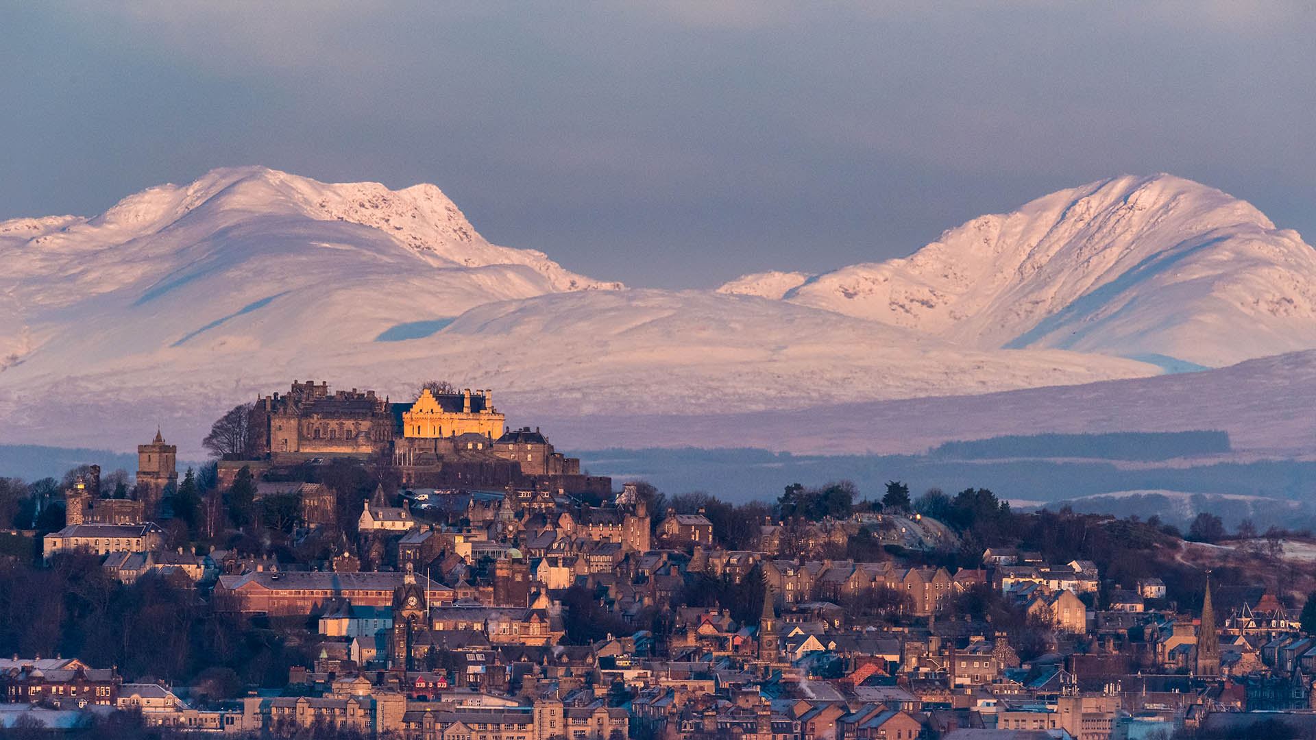 Stirling castle in winter with a dramatic, snow-capped mountain in the background
