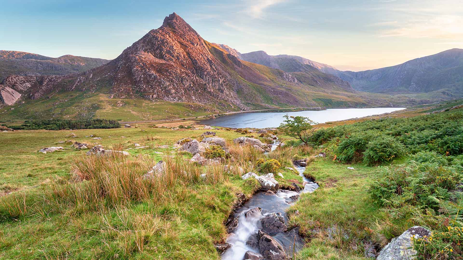 A gentle stream running into a lake belown mountains in Eryri